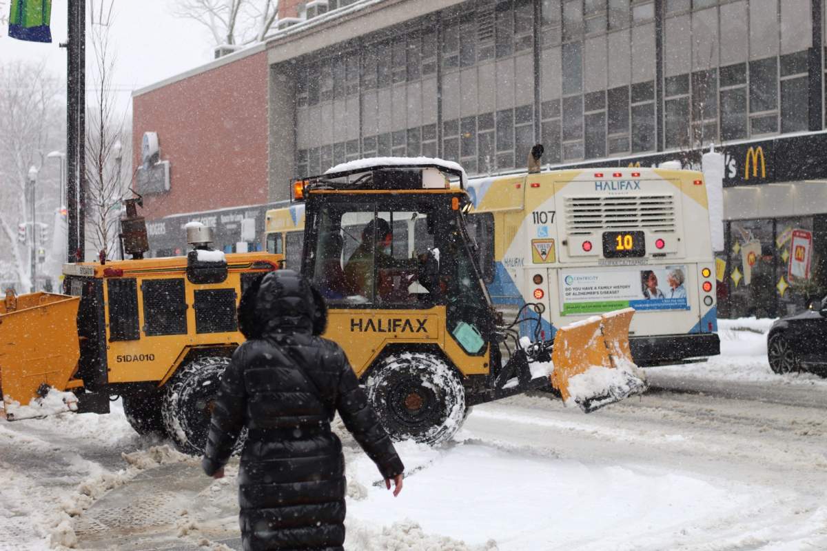 A snowplow maneuvers through foot and vehicle traffic amid heavy snowfall.