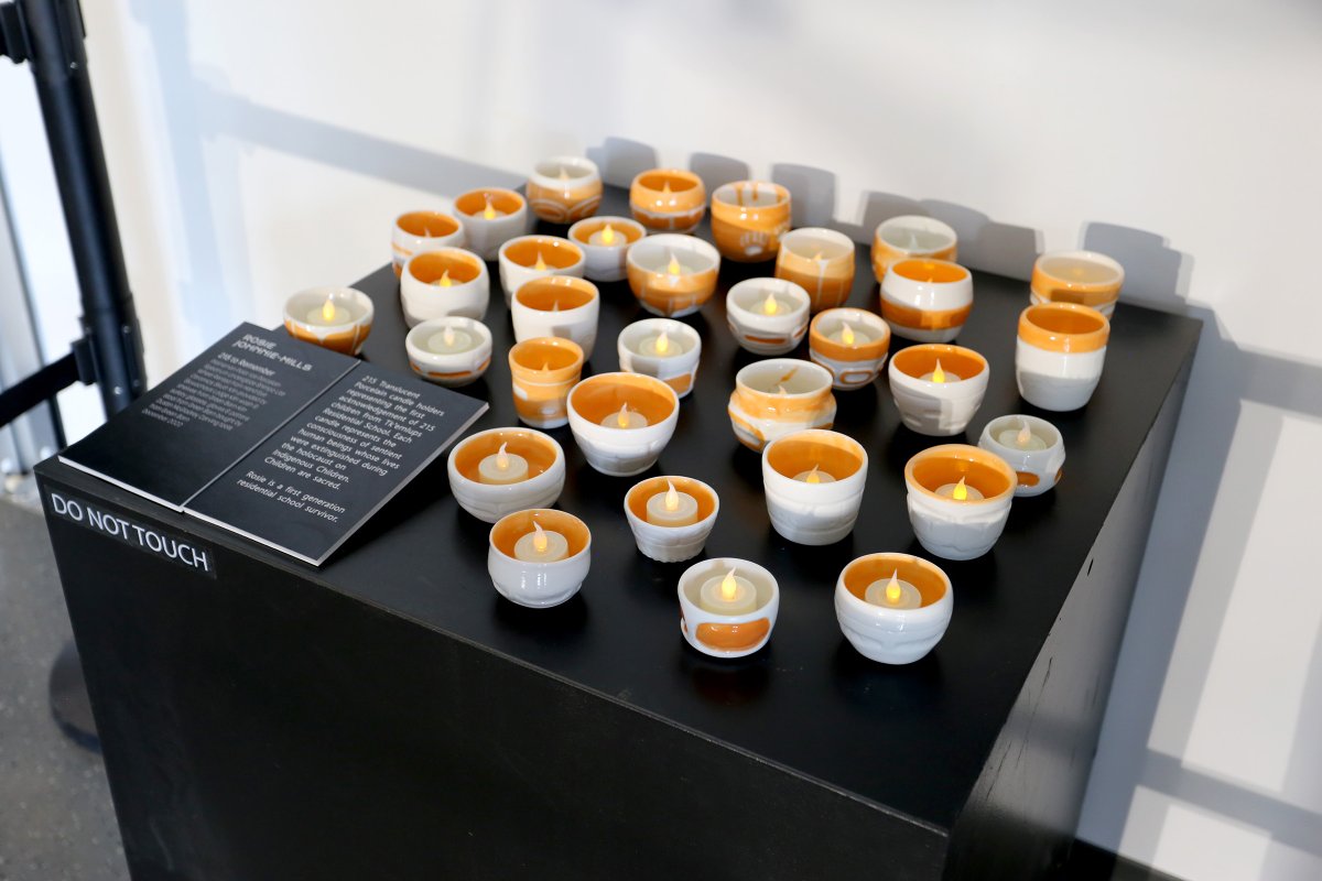 32 small pots with tealights inside are displayed on top of a black platform.