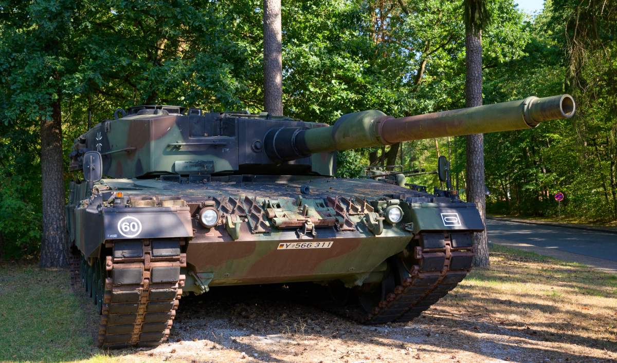 A Leopard battle tank is seen against the green forest behind it.