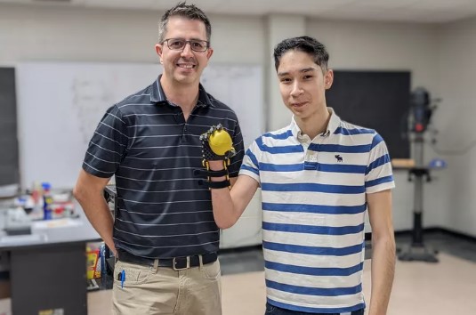 Sergio Peralta poses with engineering teacher, Jeff Wilkins, showing off the new prosthetic hand his classmates designed for him.