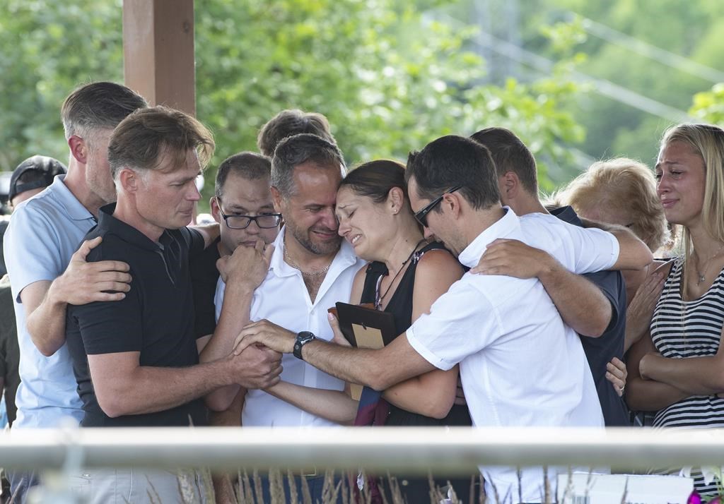 Amélie Lemieux, centre, is comforted by family members as she holds pictures of her two daughters, Romy and Norah Carpentier, at a memorial in Lévis, Que., on Monday, July 13, 2020. The maternal grandmother of two young Quebec girls killed by their father in July 2020 says he was more agitated and nervous in the lead up to killings. 