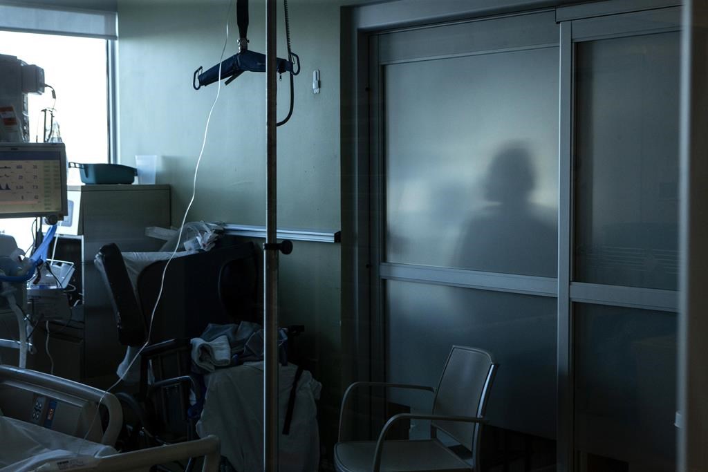 A nurse is silhouetted behind a glass panel as she tends to a patient in the intensive care unit at the Bluewater Health Hospital in Sarnia, Ont., Tuesday, Jan. 25, 2022.