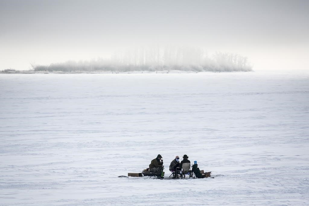 Ice fishermen huddle over a hole in the ice on Ghost Lake Reservoir near Cochrane, Alta., Sunday, Dec. 27, 2020.