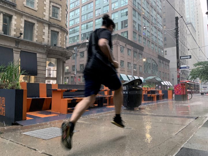 A man dashes down the sidewalk during an early summer rainstorm in Toronto on June 29, 2021, amid both heat and rainfall warnings. 