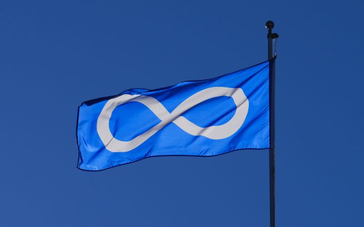 A blue and white Metis Nation flag flies in front of a bright blue sky
