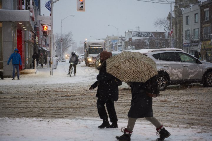 A cyclist waits at an intersection as a person with an umbrella crosses the street during a heavy winter snowstorm, Toronto, Ont., Jan. 25, 2023. 
