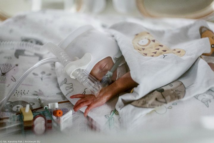 A newborn baby lies wrapped in a blanket as medical tubes provide breathing support