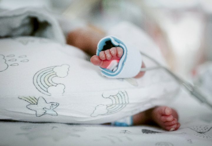 A newborn baby's feet are shown wrapped in a blanket and a hospital monitoring device