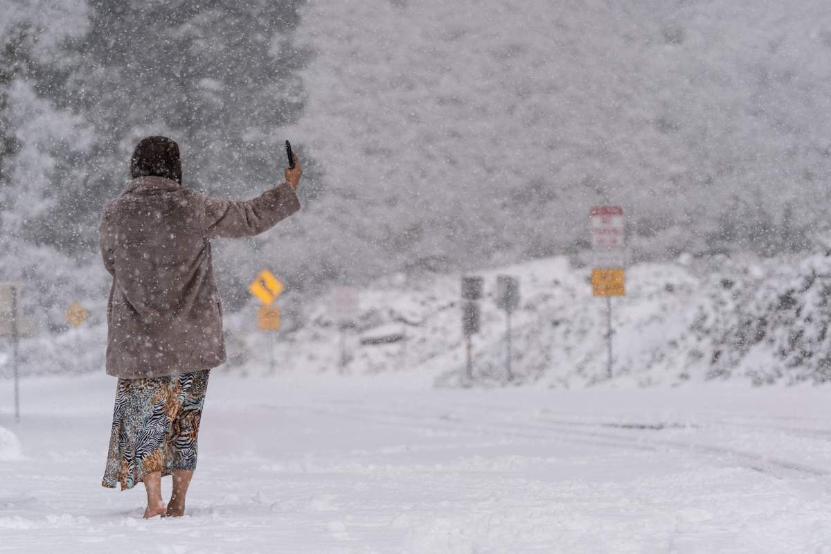 A visitor stands takes a selfie on a snow-covered road in Angeles National Forest near La Canada Flintridge, Calif., on Thursday, Feb. 23, 2023.
