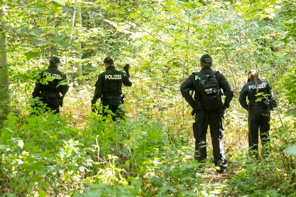 Police officers search a wooded area for clues and objects near which a female body was discovered in a passenger car on Aug. 17, 2022.
