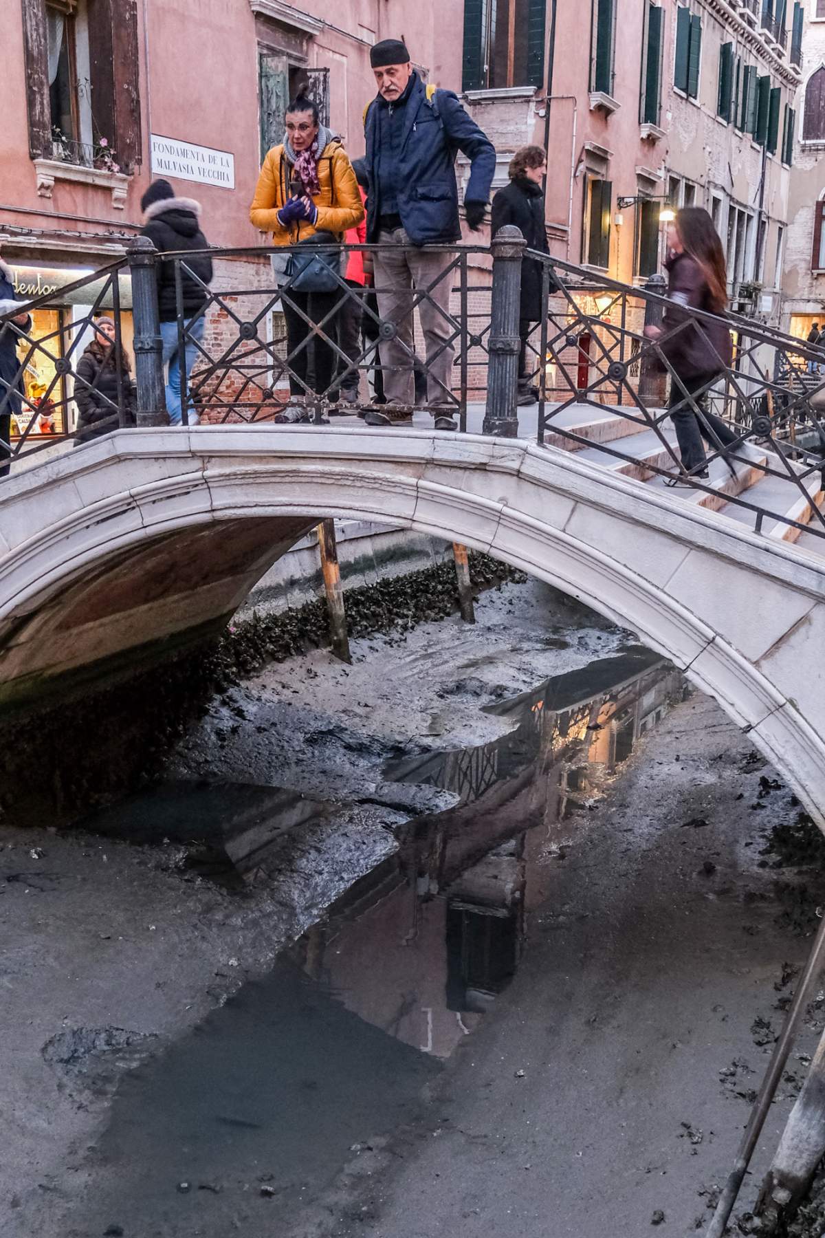 People stand on a bridge above a dried canal.