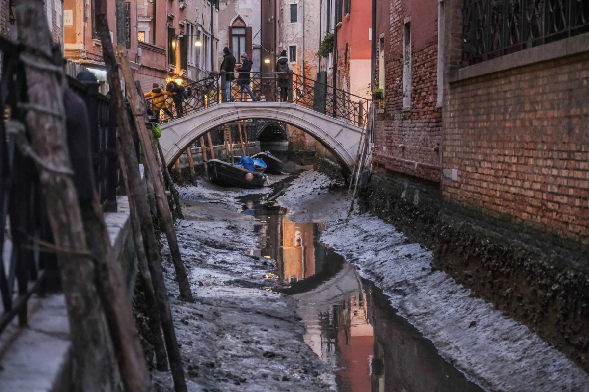 People stand on a bridge over a dried canal in Venice.