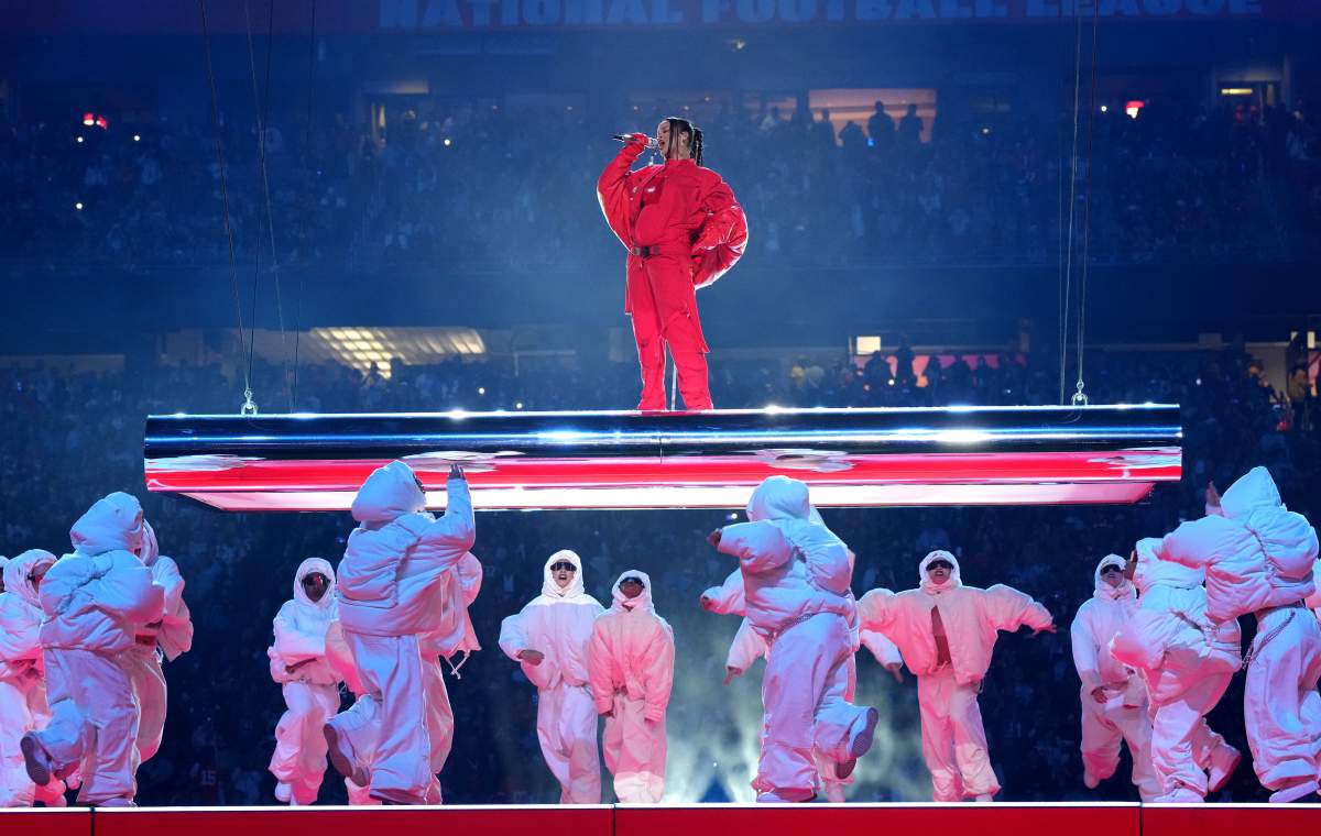 Rihanna stands on an elevated platform above several backup dancers.