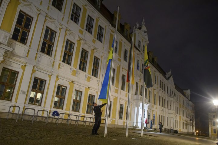 A policeman raises the flag of Ukraine in front of the state parliament of Saxony-Anhalt in Magdeburg, Germany, Friday, Feb. 24, 2023.