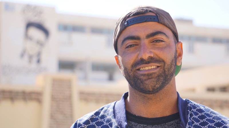 Youssef Hedfi stands next to a mural of an activist he painted on the side of a Tozeur building.