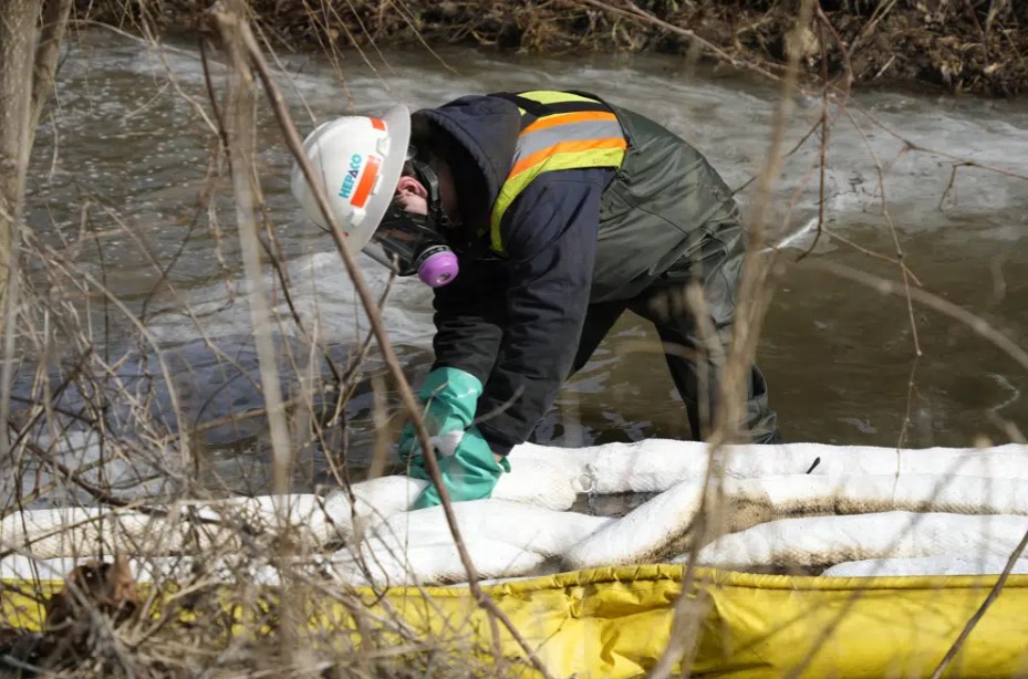 A HEPACO worker places booms in a stream in East Palestine, Ohio, on Feb. 9 as the cleanup continues after the derailment of a Norfolk Southern freight train.