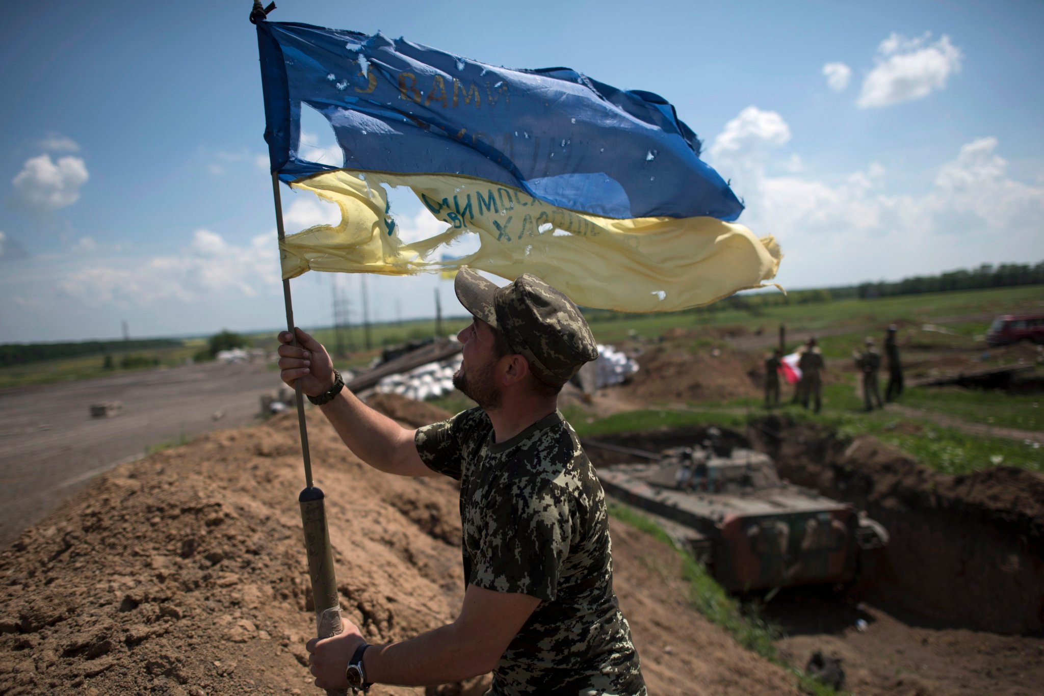 ウクライナ戦争 A tattered Ukrainian flag is stood up tall in a field.