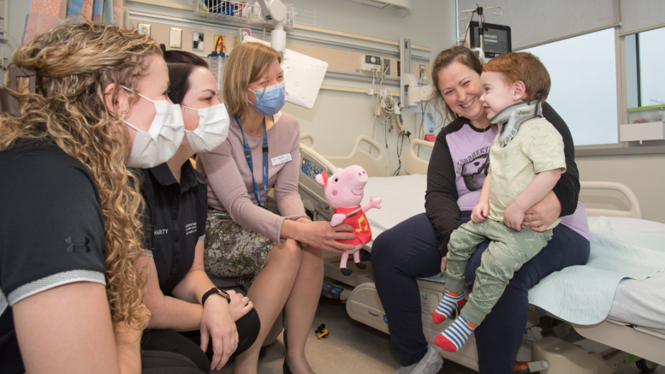 Jessi Baer and Charity Lindsay of the Children’s Hospital Neonatal Paediatric Transport Team and Dr Janice Tijssen sit beside a hospital bed while Gillian Burnett, sitting on the bed, holds her son Waylon Saunders on her lap.