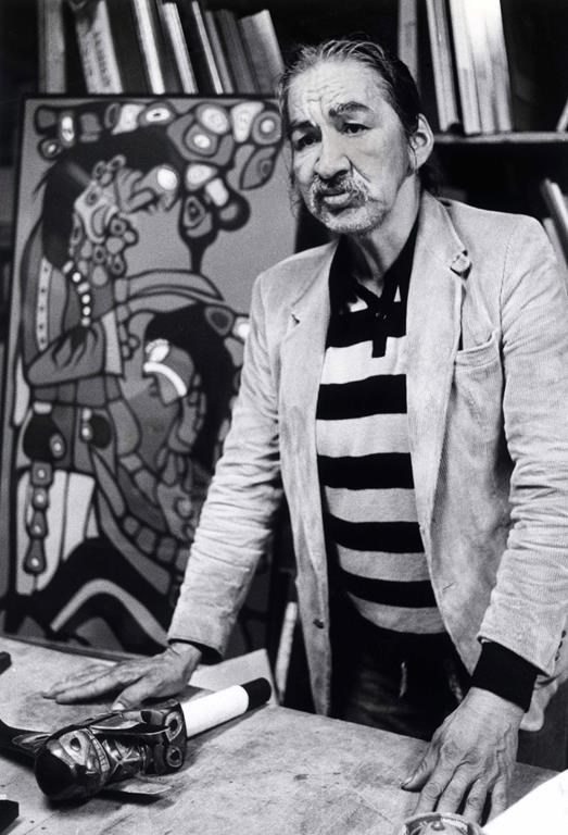 Indigenous artist Norval Morrisseau says he is heppy sketching in the streets of Vancouver as he poses in front of one of his earlier paintings at a Vancouver gallery on Monday, May 11, 1987. The OPP say they have been investigating alleged fraudulent art that is being made and sold under Morrisseau’s name.