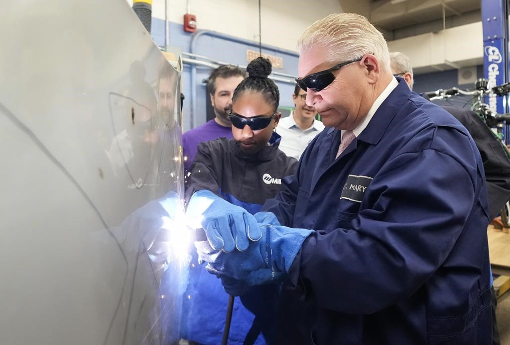 Ontario Premier Doug Ford, right, gets help from grade 11 student Shannon Williams, 16, as they practise plasma welding on a car hood as while visiting St. Mary Catholic Secondary School in Pickering, Ont., on Wednesday, March 8, 2023. Ontario will allow students in Grade 11 to begin working toward their apprenticeships in skilled trades. 