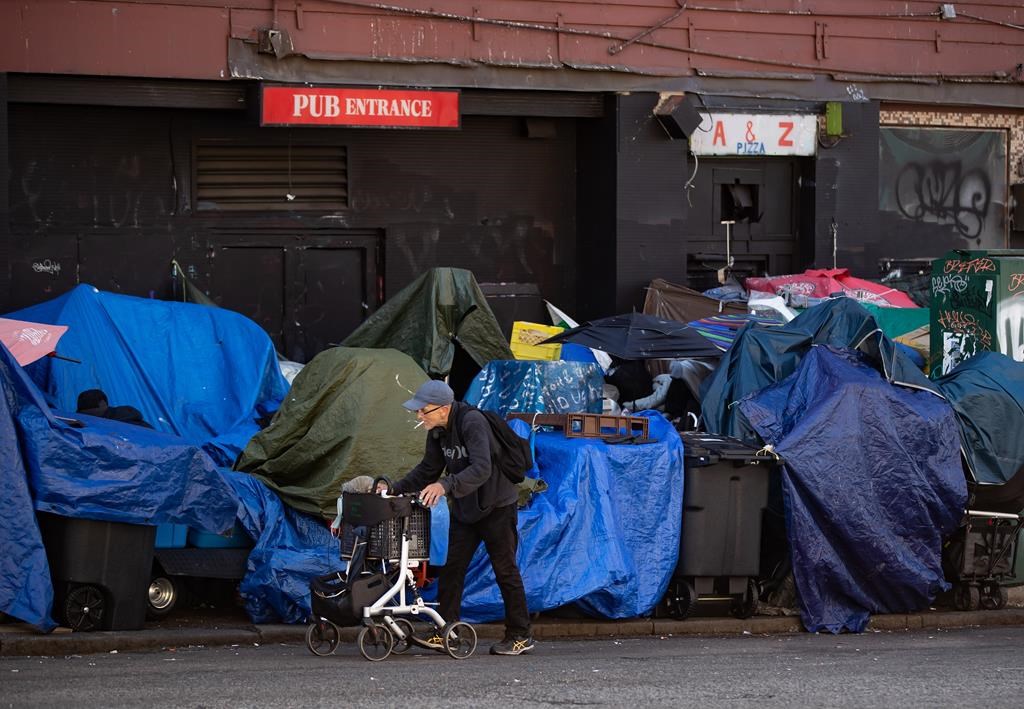A man using a rolling walker passes tents set up on the sidewalk at a sprawling homeless encampment on East Hastings Street in the Downtown Eastside of Vancouver on Aug. 16, 2022.