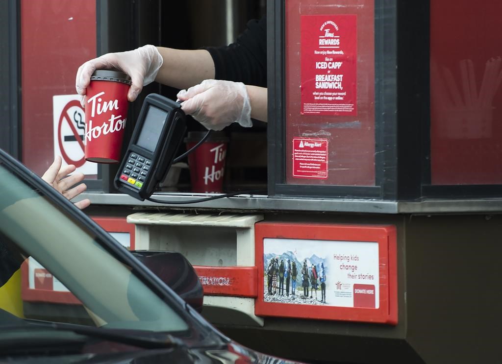 A Tim Hortons employee hands out coffee from a drive-through window to a customer.