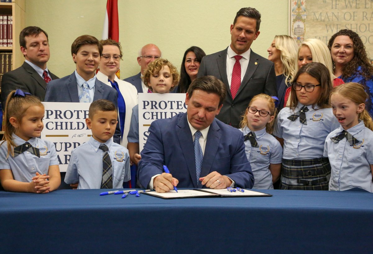 Florida Gov. Ron DeSantis signs a bill, surrounded by adults and children.