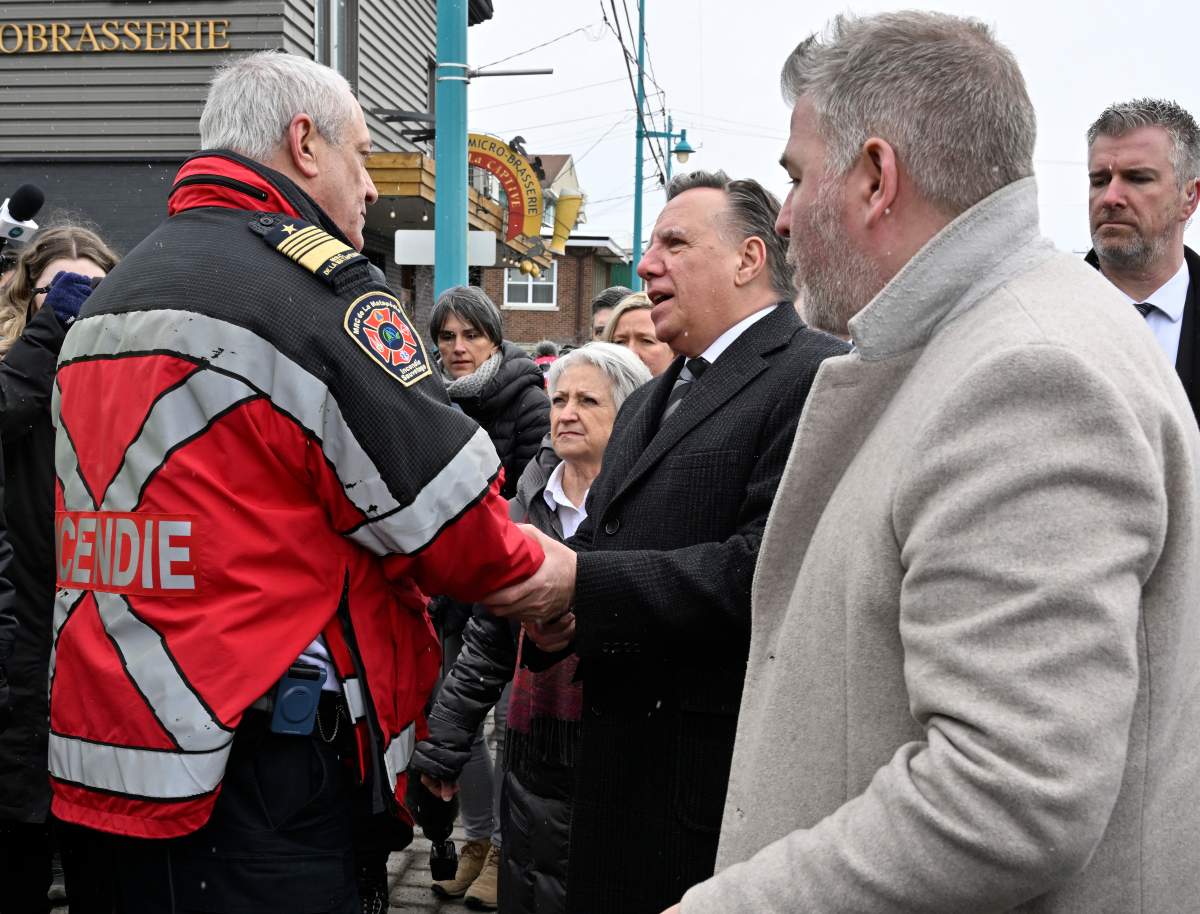 Quebec Premier François Legault, centre, speaks to a first responder, in Amqui, Que., Thursday, March 16, 2023. Local MNA Parti Quebecois MNA Pascal Bérubé, right, looks on.