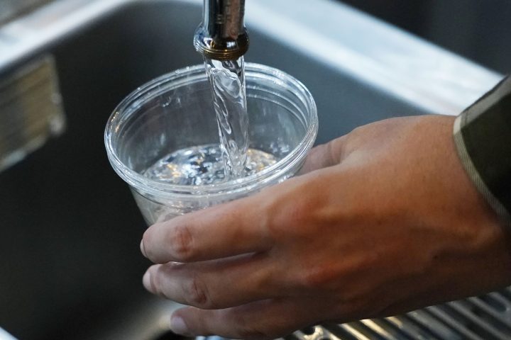 Tap water pours out of a faucet into a plastic cup held over a sink