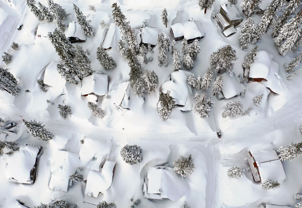 In an aerial view, snow covers roofs next to snowbanks piled up from new and past storms in the Sierra Nevada mountains, in the wake of an atmospheric river event, on March 12, 2023 in Mammoth Lakes, Calif.