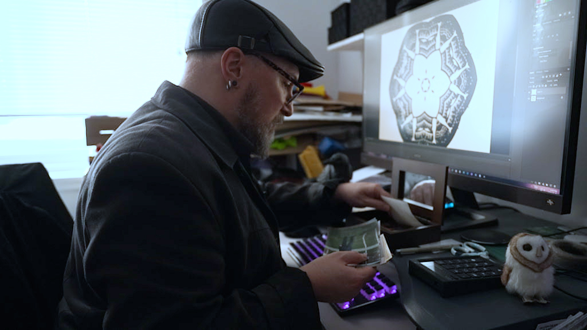 Multi-disciplinary artist and filmmaker, Glenn Gear, looks through a collection of family photos in the office of his Montreal apartment. He's in front of a computer screen, which shows some of his work, a digital medallion in black on a white background.