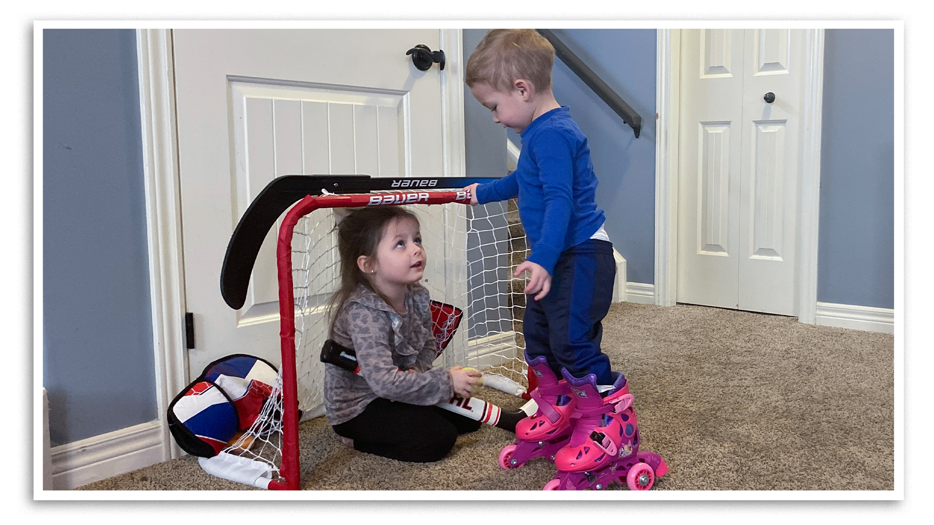 A young boy and girl play hockey with miniature sticks in the playroom of Stephen and Rebecca Krall's home in Petrolia, Ontario. The girl on the left, Grace, is kneeling between the goal posts. The boy on the right has pink skates on his feet. Grace lives with her aunt and uncle full-time, having been placed in their care by the Sarnia-Lambton Children's Aid Society.