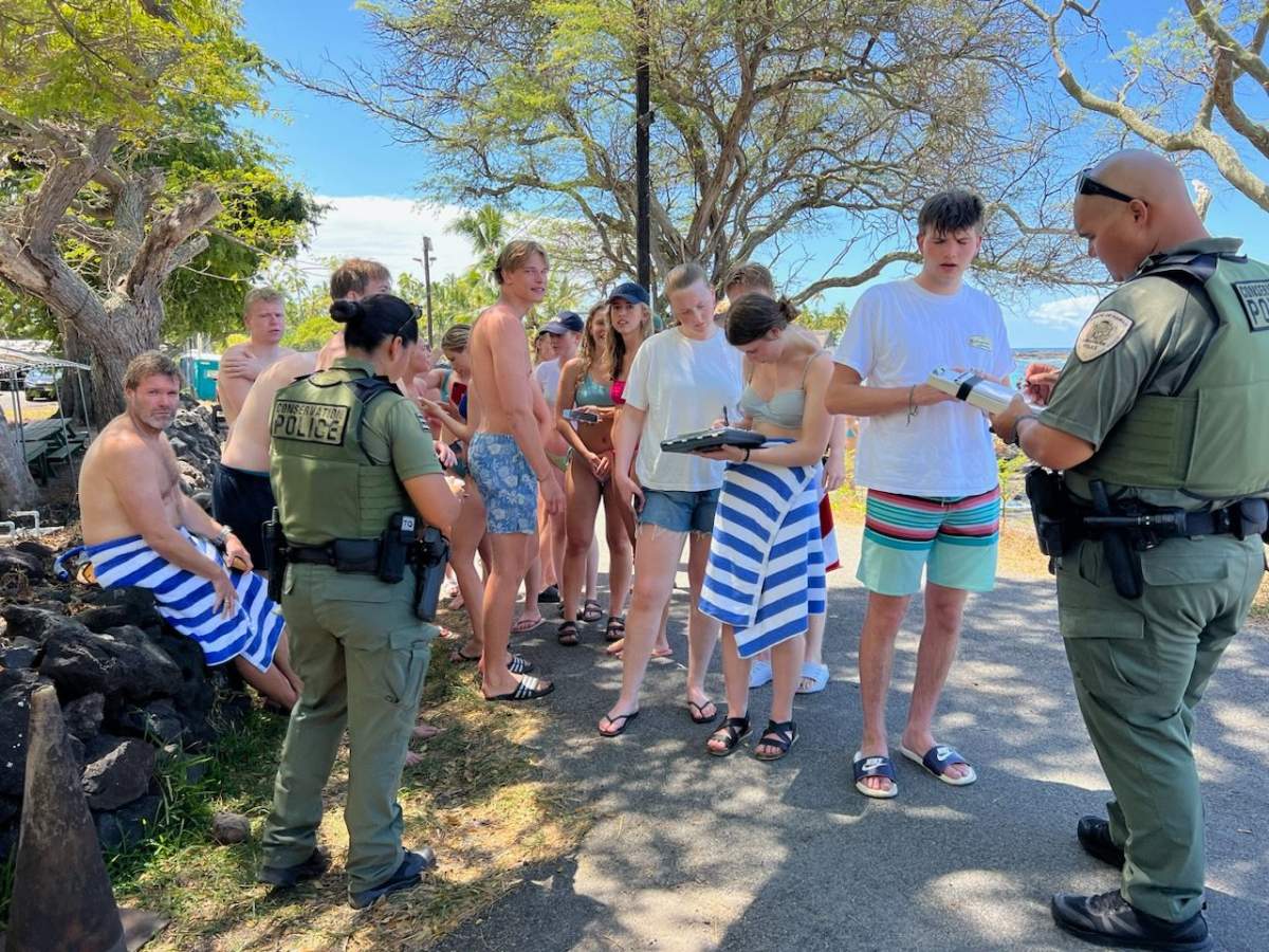 People in bathing suits stand beside uniformed officers.