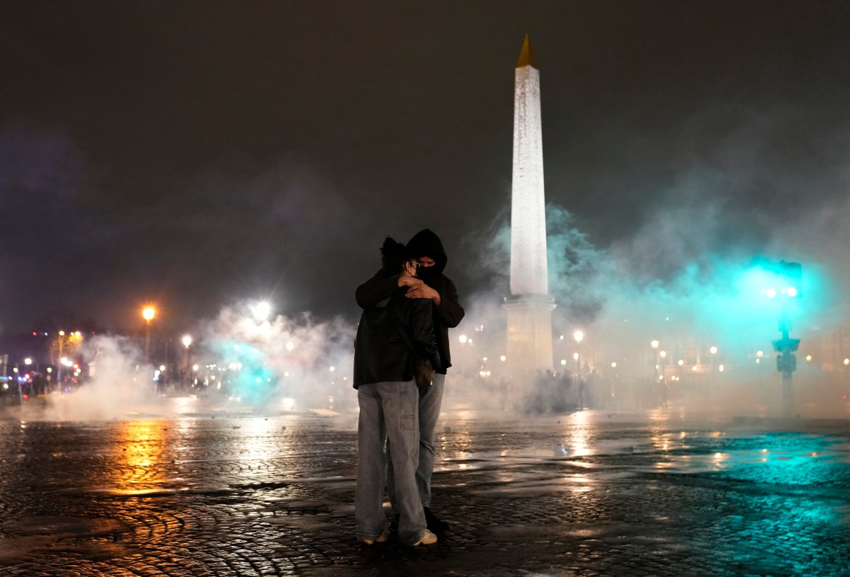 Dos personas se abrazan en medio de un remolino de gases lacrimógenos recortado por la oscuridad de la noche.