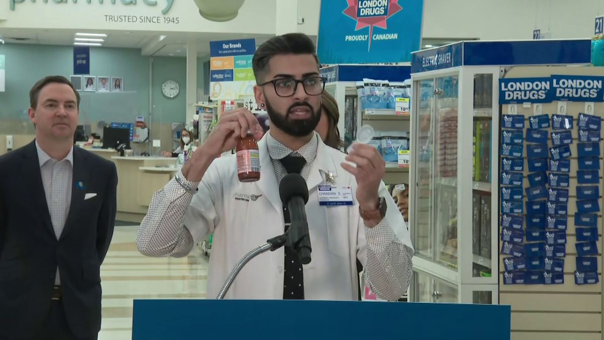 Edmonton pharmacist Chandan Sangha holds up a bottle of Turkish-manufactured kids pain medication Parol and a dosing spoon on March 20, 2023, as Health Minister Jason Copping (L) looks on.