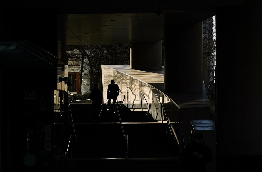 A man is silhouetted while walking up steps as sunlight reflects off a metallic wall outside an office tower in downtown Vancouver, on Thurs. March 30, 2023.