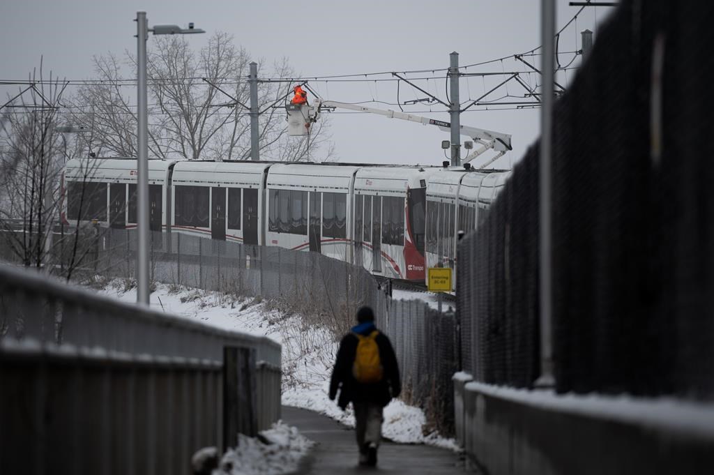 A worker repairs overhead wires on a stalled LRT OC Transpo train near Lees Ave., station in Ottawa, on Friday, Jan. 6, 2023. A severe ice storm that hit Ottawa on Wednesday night has shutdown the light rail transit system due a power outage and has left passengers stuck aboard the train. THE CANADIAN PRESS/Spencer Colby.