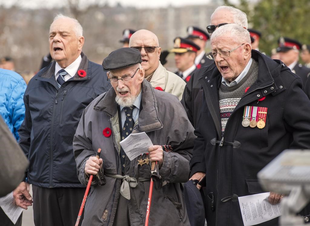 100-year-old Second World War veteran Angus Hamilton, centre, and Rev. Bob Jones, right, sing O Canada as part of the provincial Remembrance Day ceremony in Fredericton, Friday, Nov. 11, 2022. Three days before Hamilton turned 101, the Second World War veteran died peacefully at his home. THE CANADIAN PRESS/Stephen MacGillivray.