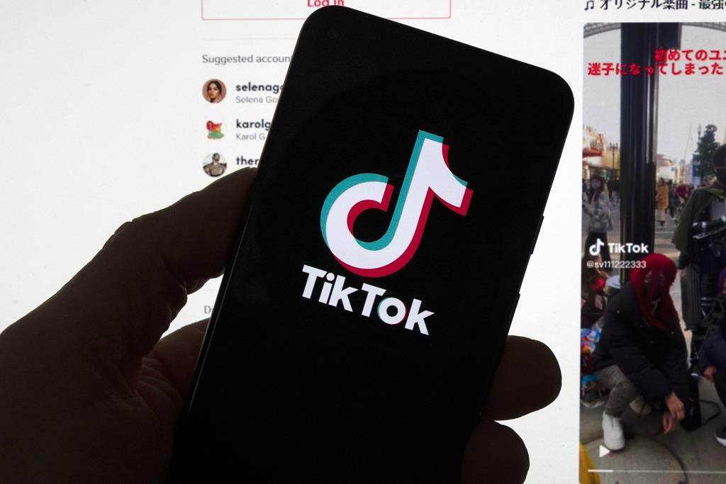 The TikTok logo is seen on a mobile phone in front of a computer screen which displays the TikTok home screen, March 18, 2023, in Boston. The CEO of TikTok dropped into a TED Talks in Vancouver to address concerns over data security on his social media platform. THE CANADIAN PRESS/AP, Michael Dwyer.