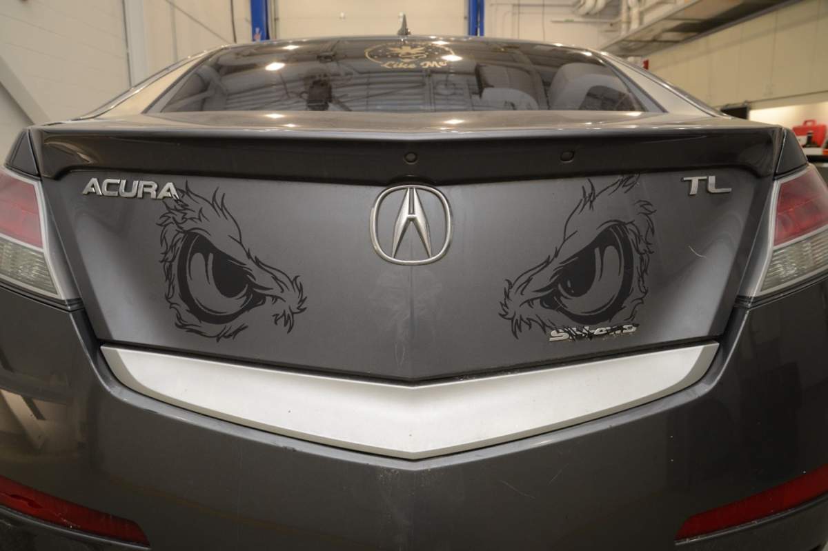 The trunk of a grey sedan with large decals of what looks like furry eyes.