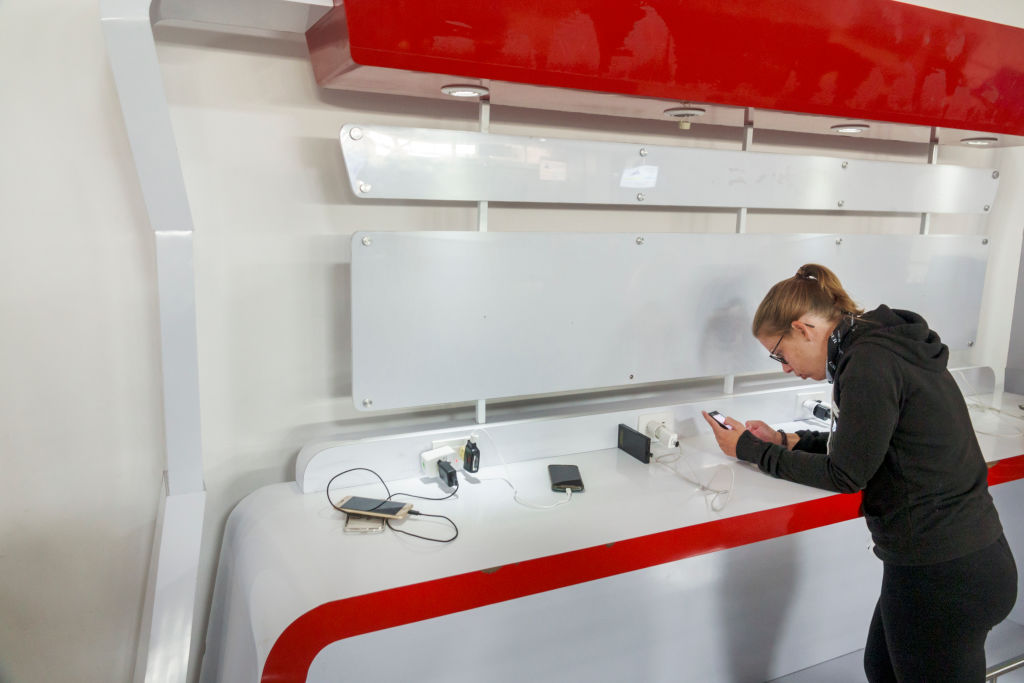 A woman charges her phone at a public charging station in an airport.