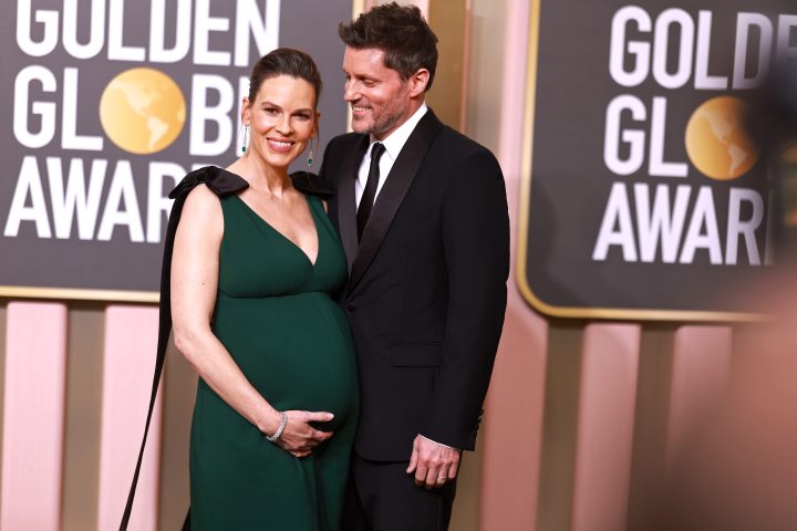 Hilary Swank and Philip Schneider on a red carpet. She wears a green dress and is visibly pregnant. He wears a black suit.