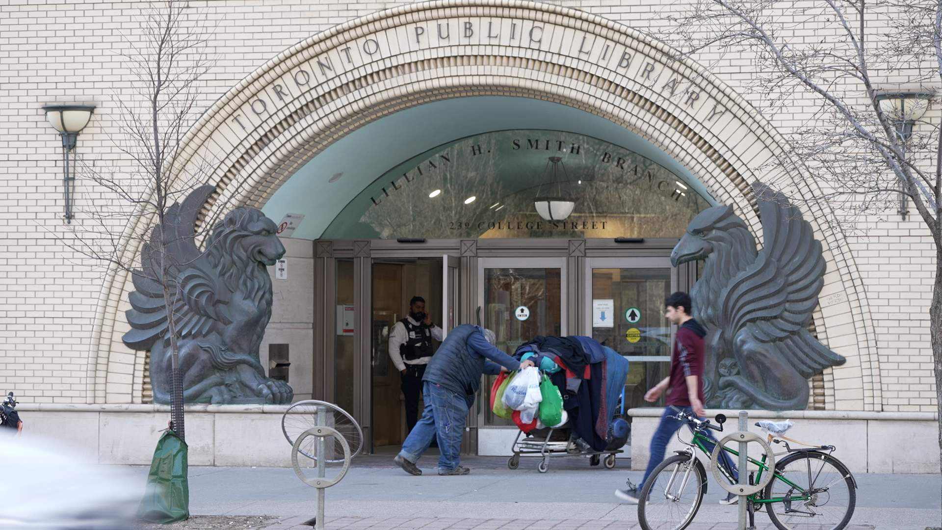 A security guard watches as man on the street wheels his belongings into a public library in Toronto
