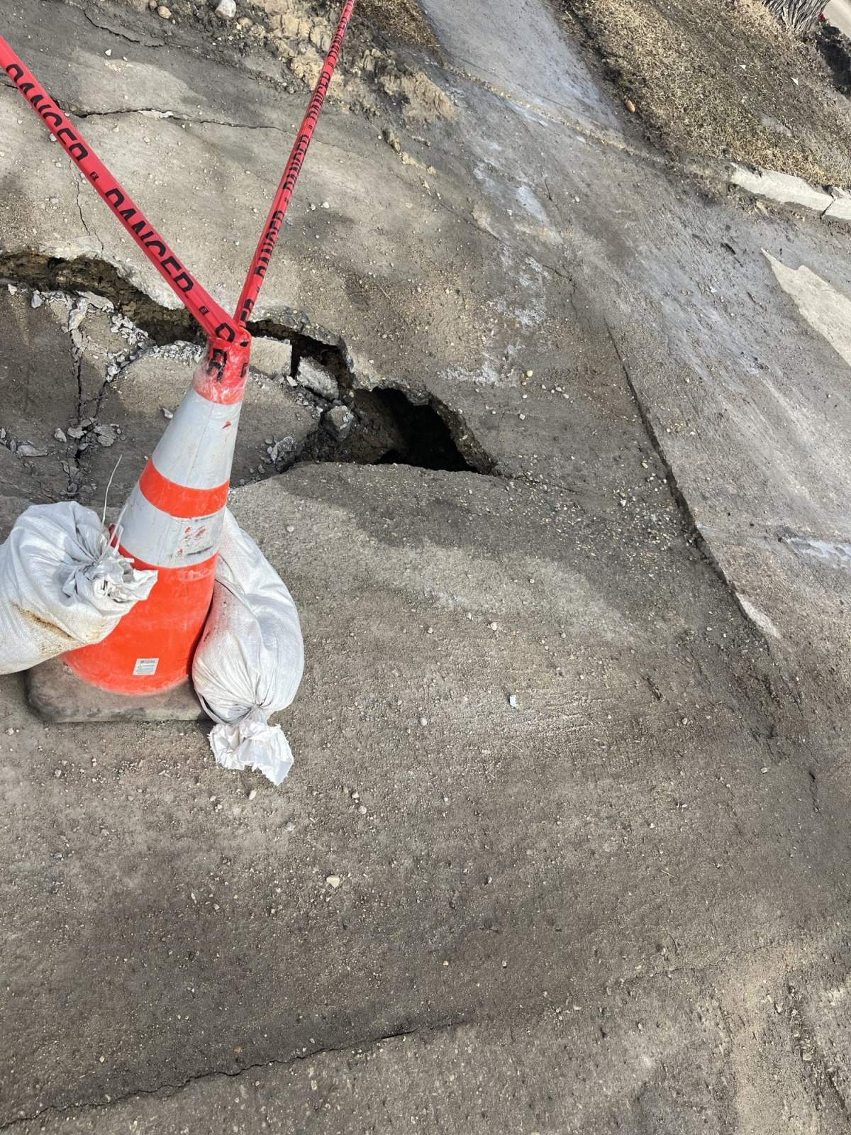 A resident put sandbags and caution tape around a City of Winnipeg cone left to mark a sinkhole.