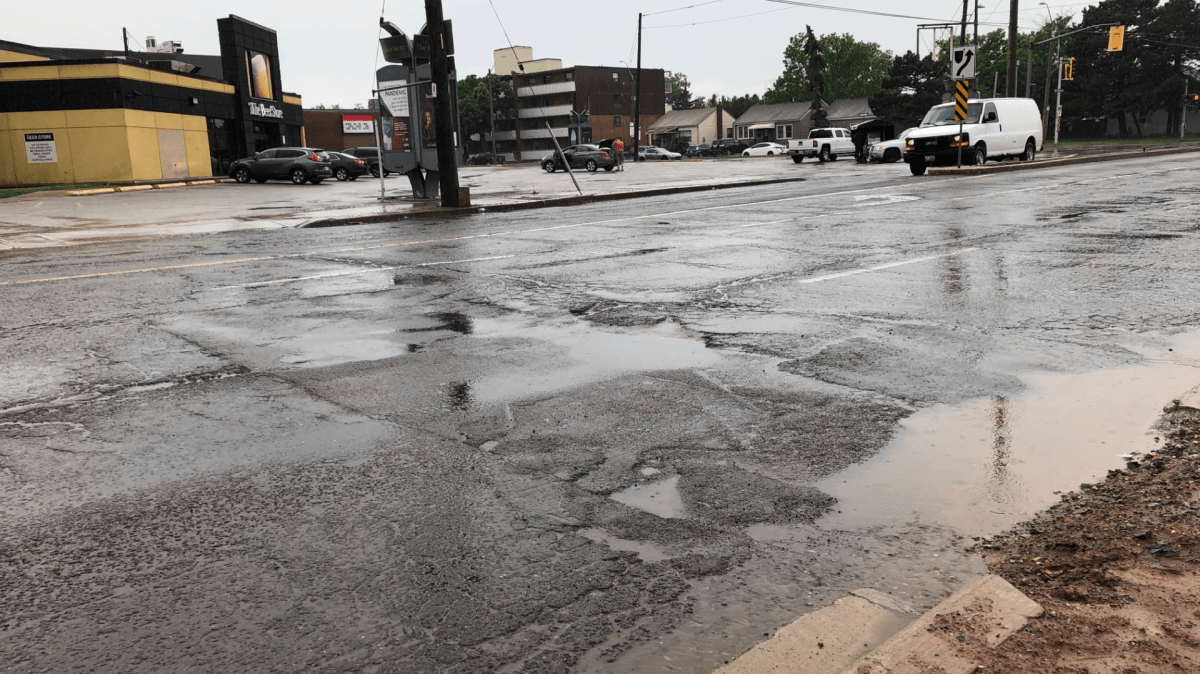 A photo of a rain-covered portion of Barton Street East, with potholes and large divots in the road.