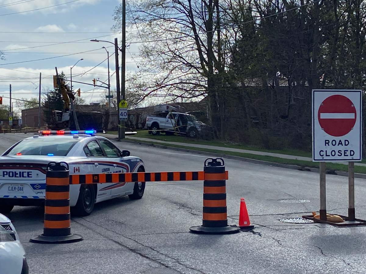 A London police cruiser is parked on the road while a truck in the background is seen on the grass past a sidewalk.