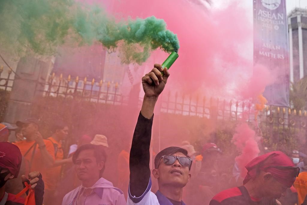 A worker holds up a smoke stick during a May Day rally in Jakarta, Indonesia, Monday, May 1, 2023.