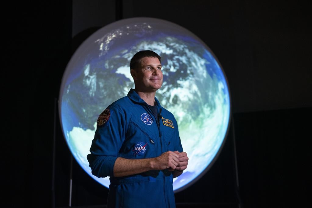 Canadian Space Agency astronaut Jeremy Hansen stands in front of a display as he participates in an interview at the opening of Earth in Focus: Insights from Space, a new exhibition at the Canada Science and Technology Museum in Ottawa, on Friday, Nov. 26, 2021. Before Hansen gets a change to plant Canada's flag on a mission to the moon next year he will carry the Canadian flag at the coronation of the country's new King. THE CANADIAN PRESS/Justin Tang.