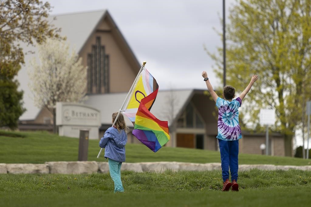 John and Sarah Barbier wave at vehicles while holding a Pride flag across the road from the Netherlands Reformed Congregation church in Norwich, Ont., protesting a recent bylaw prohibiting non-civic flags from municipal property. THE CANADIAN PRESS/Nicole Osborne.