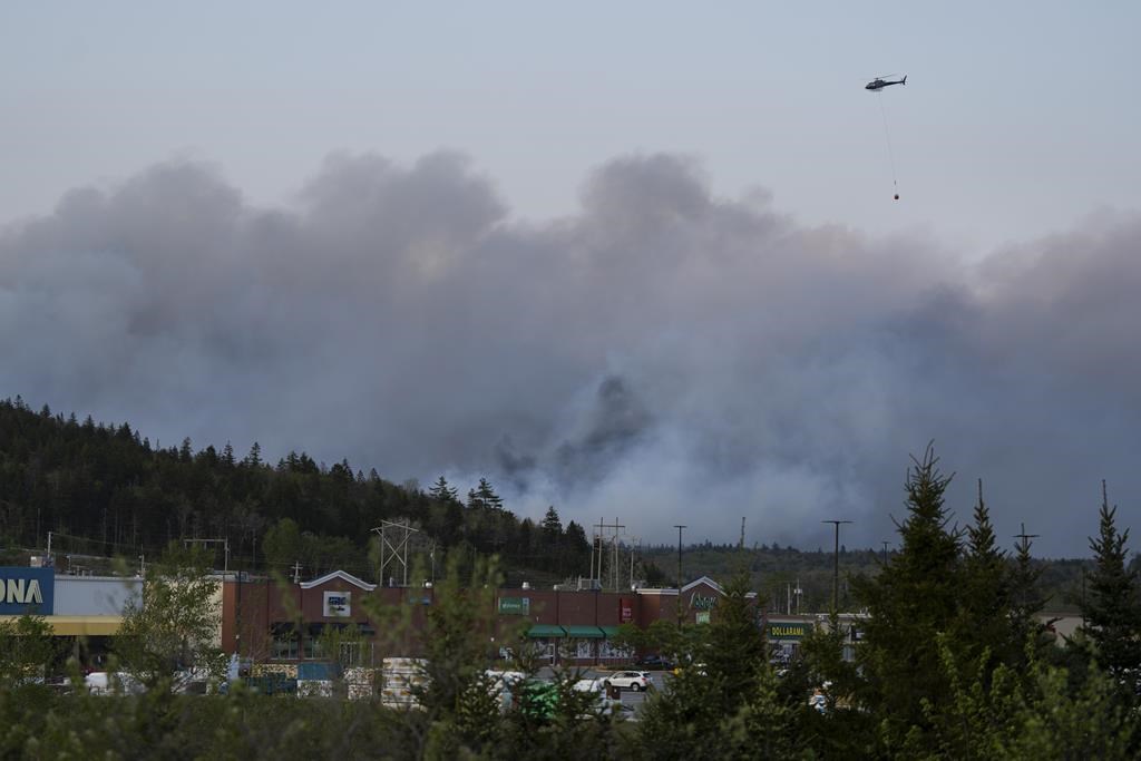 A helicopter carrying water flies over heavy smoke from an out-of-control fire in a suburban community outside of Halifax that spread quickly, engulfing multiple homes and forcing the evacuation of local residents on Sunday May 28, 2023.